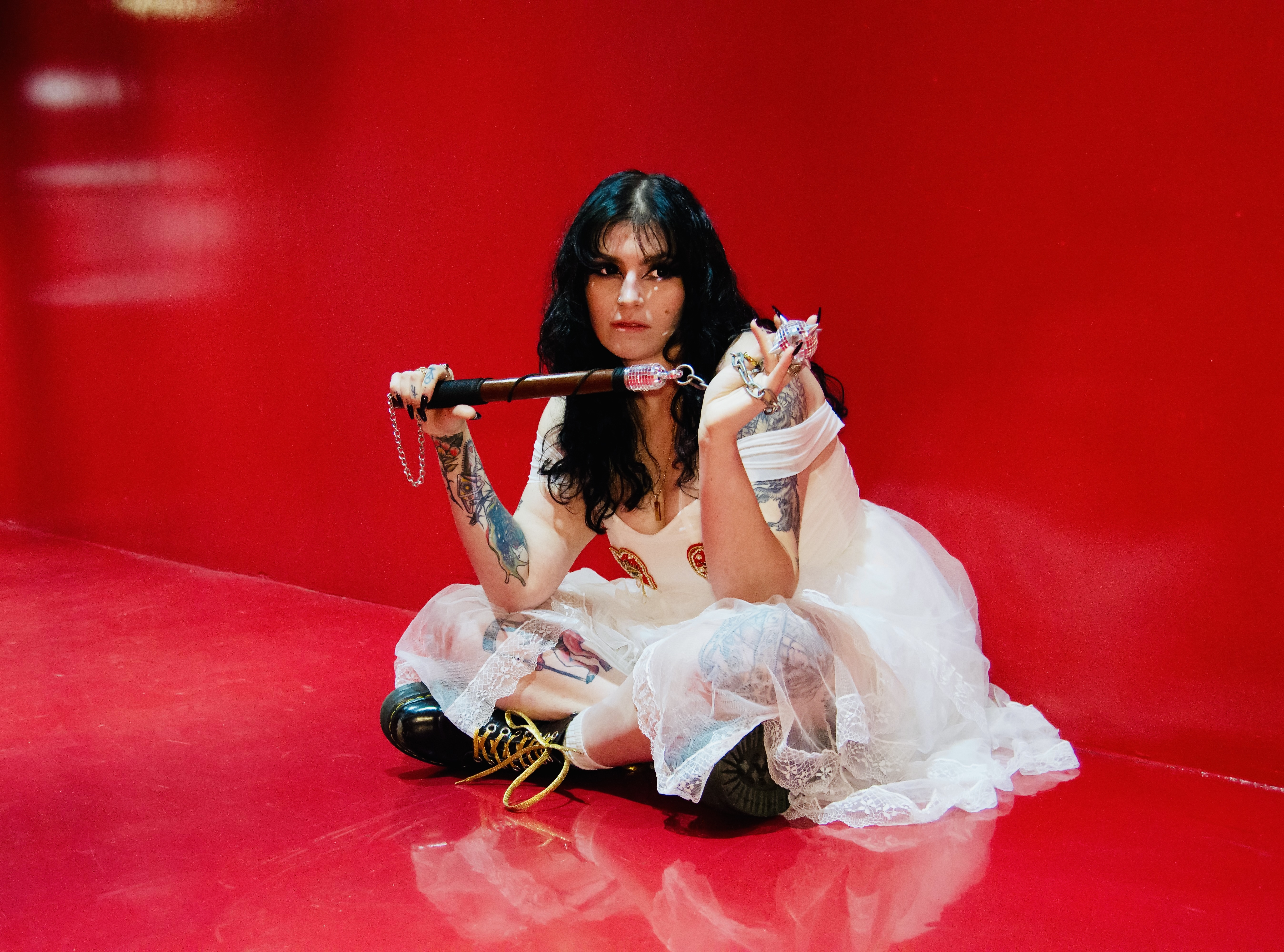 Glitchlette in a white dress with a red background holding a flail that is also a disco ball